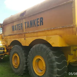 Articulated water tanker truck with a hose reel parked beside a haul truck