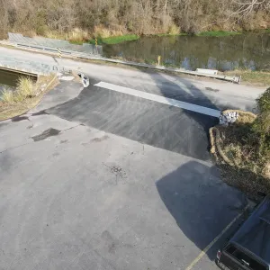 Asphalt approach and paved apron at the trail crossing, with stone and erosion socks protecting the edge