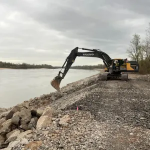 Excavator on the crest setting rock along the riverside slope under overcast sky