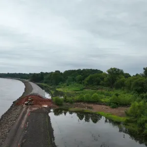 Aerial view of the riprapped embankment with a small exposed fill section and a dozer working, with a backwater channel on the landside