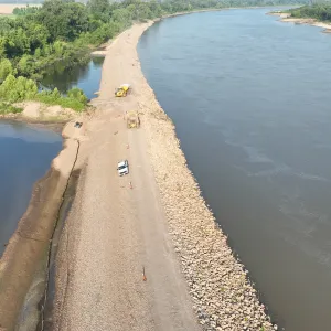 Haul trucks and a pickup on the gravel crest road, with silt fence running along the landside toe