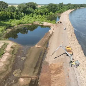 Long-reach excavator loading an articulated dump truck on the crest, with a second haul truck up-station