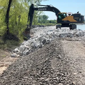 Excavator on the crest with large placed riprap on the slope and crushed rock along the access road